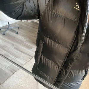 Svart vinterjacka från Haglöfs - Säljer en svart dunjacka från Haglöfs i mycket bra skick. Jackan är perfekt för vintern med sin pufferstil och långa ärmar. Den har en dragkedja framtill och en stor huva för extra värme. Supermysig och stilren för kalla dagar! 