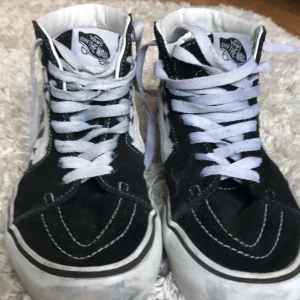 Svartvita rutiga Vans sneakers - Säljer ett par klassiska Vans sneakers i svart och vitt med coolt rutigt mönster. Skorna har snörning och är i bra skick, perfekta för skate eller vardagsbruk. De har en hög modell som ger extra stöd runt ankeln.