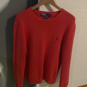 Röd stickad tröja från Polo Ralph Lauren - Säljer en snygg röd stickad tröja från Polo Ralph Lauren. Den har en klassisk design med rund hals och det ikoniska blå logotypbroderiet på bröstet. Perfekt för både höst och vinter, och den är i mycket bra skick. Passar perfekt för en stilren och avslappnad look. Inga defekter förutom lite nopprig under bröstet😃 pris kan diskuteras