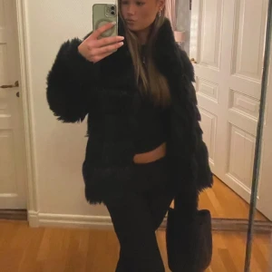 Svart pälsjacka - Snygg och trendig svart pälsjacka med långärmad design. Perfekt för att hålla sig varm och stilren under kyliga dagar. Jackan har en fluffig textur som ger en lyxig känsla.