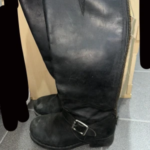 Svarta johny bulls stövlar  - Snygga svarta stövlar i skinn med dragkedja längs sidan och ett dekorativt spänne. Perfekta för höst och vinter. Johny bulls skor