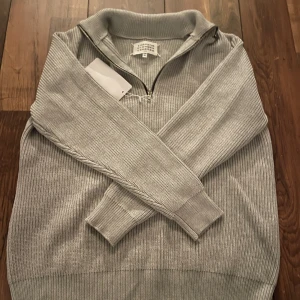   maison margiela stickad tröja - Snygg grå stickad tröja från Maison Margiela med halv dragkedja och ribbade detaljer. Perfekt för kyligare dagar. Storlek m