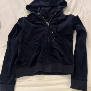 Mörkblå hoodie från Juicy Couture - Säljer en snygg och bekväm mörkblå hoodie från Juicy Couture. Den har en dragkedja framtill och en mysig huva. Perfekt för en avslappnad stil eller en kylig dag. Passar bra till jeans eller leggings. 