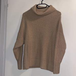 Mysig beige stickad polotröja perfekt för kyliga dagar. Den har en avslappnad passform med långa ärmar och en stor polokrage som håller dig varm och bekväm. Perfekt för både höst och vinter!