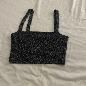Svart glittrig linnetopp från Gina Tricot - Snygg svart glittrig linnetopp från Gina Tricot i storlek S. Perfekt för festliga tillfällen med sina glittriga detaljer. Toppen har smala axelband och en tight passform. Passar perfekt till en utekväll eller fest!💕