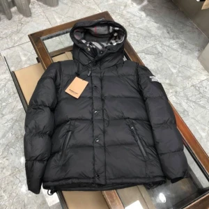 Burberry jacka - Säljer en snygg svart dunjacka från Burberry. Den har en quiltad design och en praktisk huva med mönstrat foder. Jackan är perfekt för kalla dagar och har både dragkedja och knappar framtill. Den är i mycket bra skick och redo för vintern!