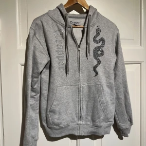 Tarapper tröja - Säljer en grå hoodie från Trapper med ett coolt ormtryck på framsidan. Perfekt för höst och vår när du vill ha något bekvämt och stilrent. 