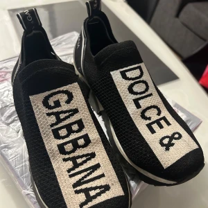 Svarta sneakers  - Snygga svarta sneakers med vit text på ovansidan. De har en modern design utan snörning och en elastisk passform. Perfekta för en stilren look både till vardags och fest. Skorna har en bekväm sula och är i mycket bra skick.