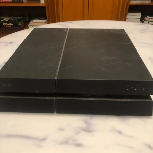 Svart PlayStation 4 med spel - Säljer en svart PlayStation 4 i gott skick. Konsolen har en stilren design med en matt finish. Medföljer flera populära spel som FIFA-serien från 10 till 23, NBA 2K18 och Call of Duty: Modern Warfare. Perfekt för spelkvällar med vänner eller soloäventyr. Allt fungerar som det ska!