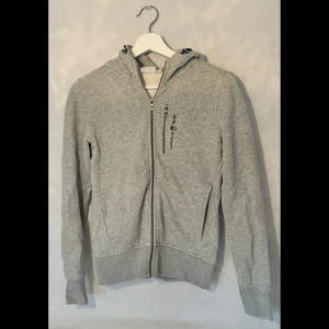 Grå zip hoodie från Sail Racing - Säljer en snygg grå hoodie från Sail Racing i storlek XS. Den har en dragkedja framtill och en praktisk bröstficka med logga. 