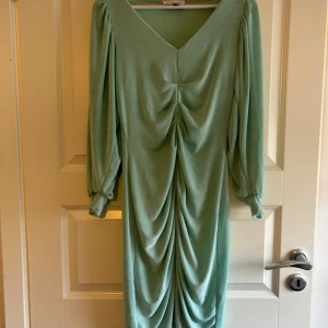 Mintgrön klänning med rynkdetaljer - Snygg mintgrön klänning med långa ärmar och v-ringning. Klänningen har rynkdetaljer framtill som ger en elegant touch. Perfekt för speciella tillfällen. Använd två gånger.