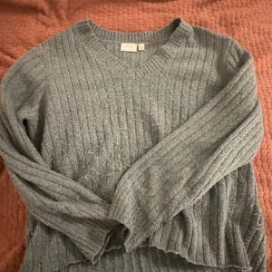 Grå ribbad tröja från VILA - Säljer en mysig grå ribbad tröja från VILA. Tröjan har en v-ringad hals och långa ärmar, perfekt för kyligare dagar. Den är både stilren och bekväm, idealisk för en avslappnad look.