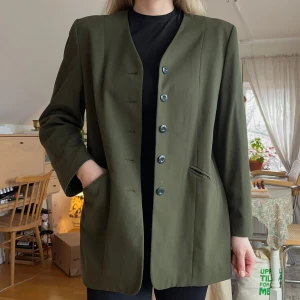 Olivgrön kavaj från Kappahl - Vintage olivgrön kavaj från Kappahl med en stilren design. Kavajen har knappar framtill och två fickor. 