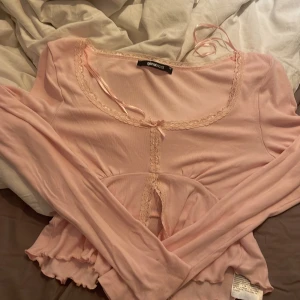 Rosa långärmad topp från Ginatricot  - Säljer en söt rosa långärmad topp från Ginatricot. Toppen har spetsdetaljer runt halsringningen och en knytning framtill. Den är lätt och bekväm, perfekt för vår och sommar. Använd en gång, inga defekter. Pris kan diskuteras!