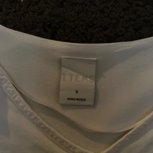 Vit blus från Vero Moda - Säljer en stilren vit blus från Vero Moda med volangdetalj framtill. Blusen har långa ärmar och en v-ringad hals. Perfekt för en elegant look.