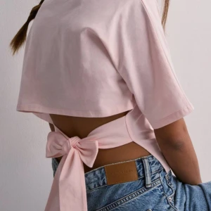 Rosa croppad topp med knyt - Säljer en söt rosa croppad topp med knyt i ryggen. Toppen har korta ärmar och en stilren design.