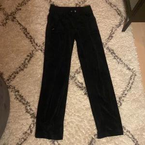 Svarta byxor från Juicy Couture - Säljer ett par svarta byxor från Juicy Couture i storlek S. Byxorna är i mjukt material och har en stilren design med små detaljer som knappar på fickorna. Perfekta för en avslappnad men ändå chic look. Passar bra till både vardag och fest!
