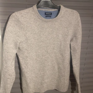 Grå ulltröja från McNeal - Säljer en stilren grå tröja från McNeal i ren lammull. Tröjan har en rund halsringning och långa ärmar, perfekt för kyligare dagar. Den är mjuk och bekväm med en diskret broderad logga på bröstet. Storlek M men den sitter som s