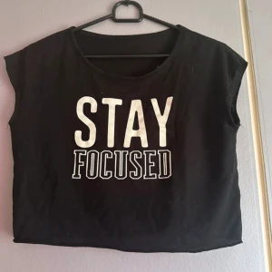 Svart croppad t-shirt med tryck - Snygg svart croppad t-shirt med texten 'STAY FOCUSED' i vitt. Perfekt för en avslappnad stil. T-shirten har korta ärmar och en rund halsringning. OBS varan finns på andra sälj sidor också så skynda att fynda innan någon annan gör de!💕