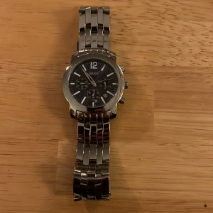 Silverfärgad klocka från Origo - Snygg silverfärgad klocka från Origo med svart urtavla och tydliga vita markeringar. Klockan har en robust metallarmband och flera funktioner på uret. Den är helt sprillans ny. Hör av er vid frågor.