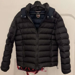 Svart pufferjacka från Colmar - Säljer en svart pufferjacka från Colmar med dragkedja och huva. Jackan är quiltad och har en stilren design, perfekt för kyligare dagar. Den är både snygg och funktionell. Pris inte hugget i sten.