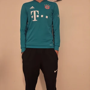 Blå långärmad fotbollströja från Adidas - Säljer en blå långärmad fotbollströja från Adidas med FC Bayern München-logga på bröstet och text på ryggen. Tröjan har vita detaljer och är perfekt för fans av laget. Passar bra för träning eller som supportertröja.