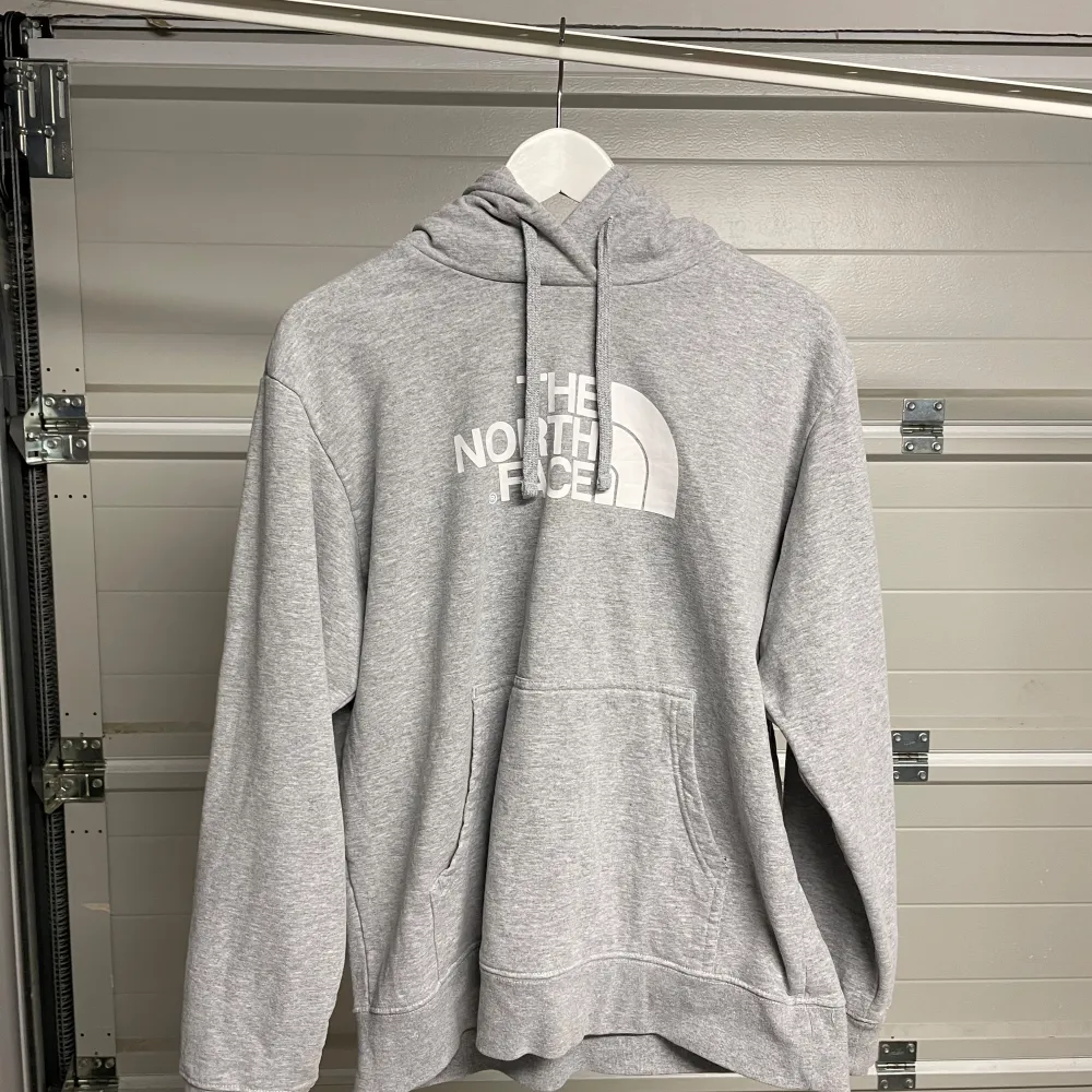 Säljer en grå hoodie från The North Face i bra skick. Den har en klassisk passform med en stor logga på framsidan. Perfekt för kyliga dagar eller som ett extra lager. Den har en känguruficka och justerbar huva med snören. Superbekväm och stilren! Säljes i befintligt skick. Storlek: L. Tröjor & Koftor.