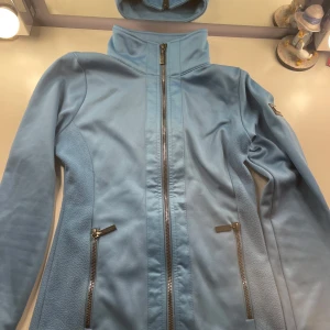 Ljusblå tjocktröja från Equestrian Stockholm  - Snygg ljusblå tjocktröja från Equestrian Stockholm med dragkedja framtill och två praktiska fickor. Perfekt för ridning eller en avslappnad dag ute. Jackan har en hög krage och broderad logga på ryggen. Den är i bra skick och bara använd en gång då den var för liten för mig, köpte från Plick men den var endast använd ett fåtal gånger när jag köpte den. Har två små fläckar men de är knappt synbara. Pris kan diskuteras. Köpare står för frakten. 