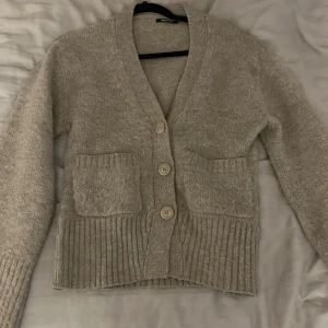 Beige kofta från Gina Tricot - Mysig beige kofta från Gina Tricot i storlek XS. Den har en ribbad nederkant och muddar, samt tre stora knappar framtill. Perfekt för kyliga dagar!