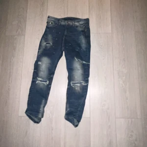 Blå jeans med slitningar och dragkedja - Snygga blå jeans från Suply and demand med coola slitningar och en dragkedja på fickan. Perfekta för en avslappnad stil med en touch av edge. De har en klassisk femficksdesign och är tillverkade i ett slitstarkt material.