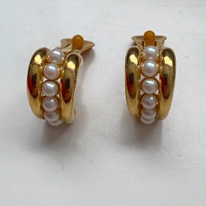 Guldörhängen med pärlor - Eleganta guldörhängen med en rad vita pärlor. De är clipsörhängen och har en rundad form som ger en klassisk look. Perfekta för att lägga till en touch av lyx till din stil. Okänd metall 