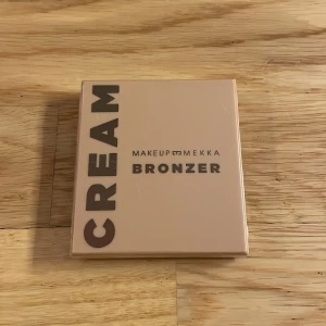Cream Bronzer från Makeup Mekka - Snygg cream bronzer från Makeup Mekka i nyansen Warm Breeze. Perfekt för att ge ansiktet en solkysst look. Kompakt förpackning som är lätt att ta med sig. Helt oöppnad.