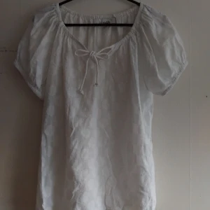 Vit blus - En vit blus från Isolde med korta puffärmar och knytband vid urringningen. Luftig men inte genomskinlig, blommigt diskret mönster. Inte använd, köpt secondhand 