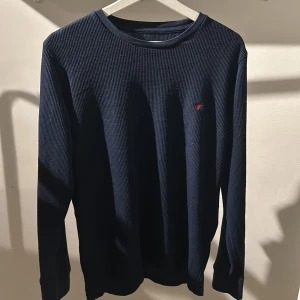Mörkblå tröja från Ralph Lauren - Säljer en stilren mörkblå tröja från Ralph Lauren. Tröjan är ribbad med långa ärmar och har en liten broderad logga på bröstet. Perfekt för en klassisk och avslappnad look. Skick 7/10 inga stora tecken på användning men den är lite uttöjd,urtvättad och så finns de små tecken på användning men inget man ser eller tänker på😁. Hör av dig!