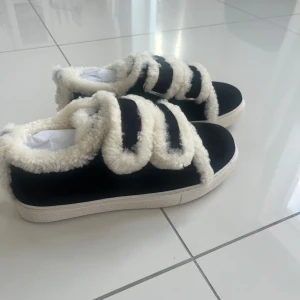 Svarta sneakers med vita pälsdetaljer-likt Inuikiis - Snygga svarta sneakers med mjuka vita pälsdetaljer. Oanvända men känns väldigt mjuka och sköna. Storlek 38