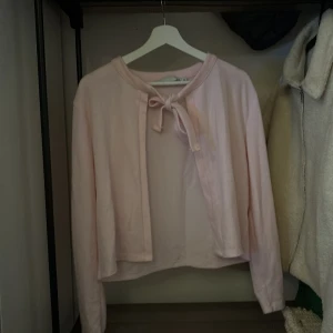 Ljusrosa kofta från 157 - Säljer en söt ljusrosa kofta från 157 i storlek M. Koftan har långa ärmar och en knytning framtill som ger en fin detalj. Perfekt för lager-på-lager-stil.