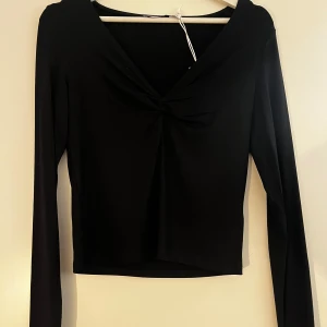 Svart långärmad topp - Snygg svart långärmad topp med en elegant knutdetalj framtill. Perfekt för en stilren look. Tillverkad i mjukt och bekvämt material.