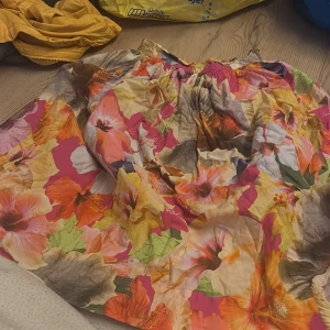 Blommig kjol från Molo - Färgglad blommig kjol från Molo i storlek 134/140. Kjolen har ett livfullt mönster med blommor i rosa, orange, gul och grön. Perfekt för att lysa upp garderoben!