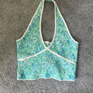 Blommig halterneck topp från Zara - Snygg blommig halterneck topp från Zara i grönt och blått med vita kanter. Toppen har en djup v-ringning och knappar bak. 