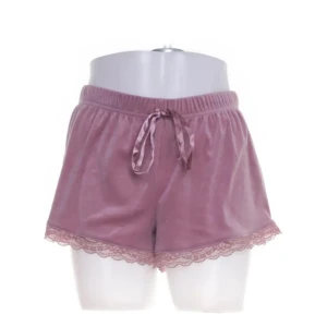 Rosa sammetsshorts, Hunkemöller - Ett par mjuka och bekväma rosa sammetsshorts från Hunkemöller. De har en söt spetsdetalj vid bensluten och ett knytband i midjan för justerbar passform. Perfekta för en avslappnad dag hemma.