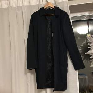 Svart rock i bomull - Snygg svart rock i 100% bomull med klassisk design. Rocken har långa ärmar och en stilren krage. Perfekt för höst och vår, med en elegant passform som passar till många tillfällen.