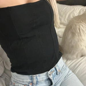 Svart korsett body - Snygg svart korsett med smala axelband. Perfekt för att skapa en stilren look. Passar bra till både jeans och kjol. Bodyn är ny men har en liten spricka efter att ha provat den flera gånger men det har inte passat min smak går enkelt att sy ihop de lilla annars fel fri😊😍