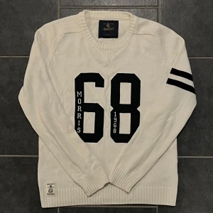 Vit tröja från Morris - Säljer en vit tröja från Morris med svart tryck '68' och text på framsidan. Tröjan har ribbade muddar och en rund halsringning. Tillverkad i 100% bomull, perfekt för en avslappnad stil.