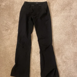 Svarta byxor från Bik Bok - Snygga svarta  lågmidjade kostymbyxor från Bik Bok med en klassisk design. De har en rak passform och är perfekta för en stilren look. De har en enkel slit längst ner på vardera ben. 