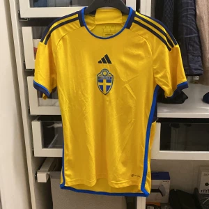 Sverige fotbollströja från Adidas - Säljer en gul fotbollströja från Adidas med blå detaljer och Sveriges emblem på bröstet. Tröjan i mycket bra skick och är knappt använd. Storlek S.