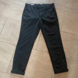 Svarta byxor från Jack & Jones - Snygga svarta byxor från Jack & Jones i modellen Slim Marco. Byxorna har en slim passform med knappar och dragkedja i midjan. Perfekta för en stilren look.