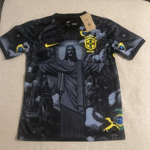 Svart Brasilien fotbollströja Neymar Jr - Snygg svart Brasilien fotbollströja från Nike med Neymar Jr och nummer 10 på ryggen. Tröjan har ett unikt mönster med Kristusstatyn och brasilianska symboler. Den är kortärmad och har gula detaljer samt Brasilien-emblem på bröstet.
