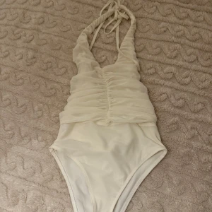 Vit bodysuit - Elegant vit bodysuit med knytband i nacken och rynkad detalj framtill. 