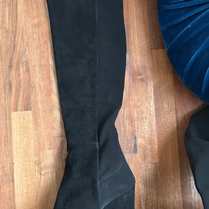 Svarta stövlar från Stuart Weitzman - Snygga svarta stövlar från Stuart Weitzman i mocka och delvis strechiga i skaftet för att smita åt ordentligt. Perfekta för en stilren look med en spetsig tå och kilklack. Knappt använda. Ordentliga sula som inte glider. För smala fötter. Nypris 8950kr.