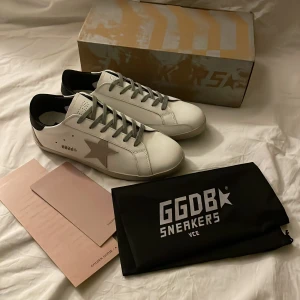 Vita sneakers från GGDB - Snygga vita sneakers från GGDB med en stjärndetalj på sidan. Skorna har grå snörning och en svart häl. Perfekta för en stilren look.